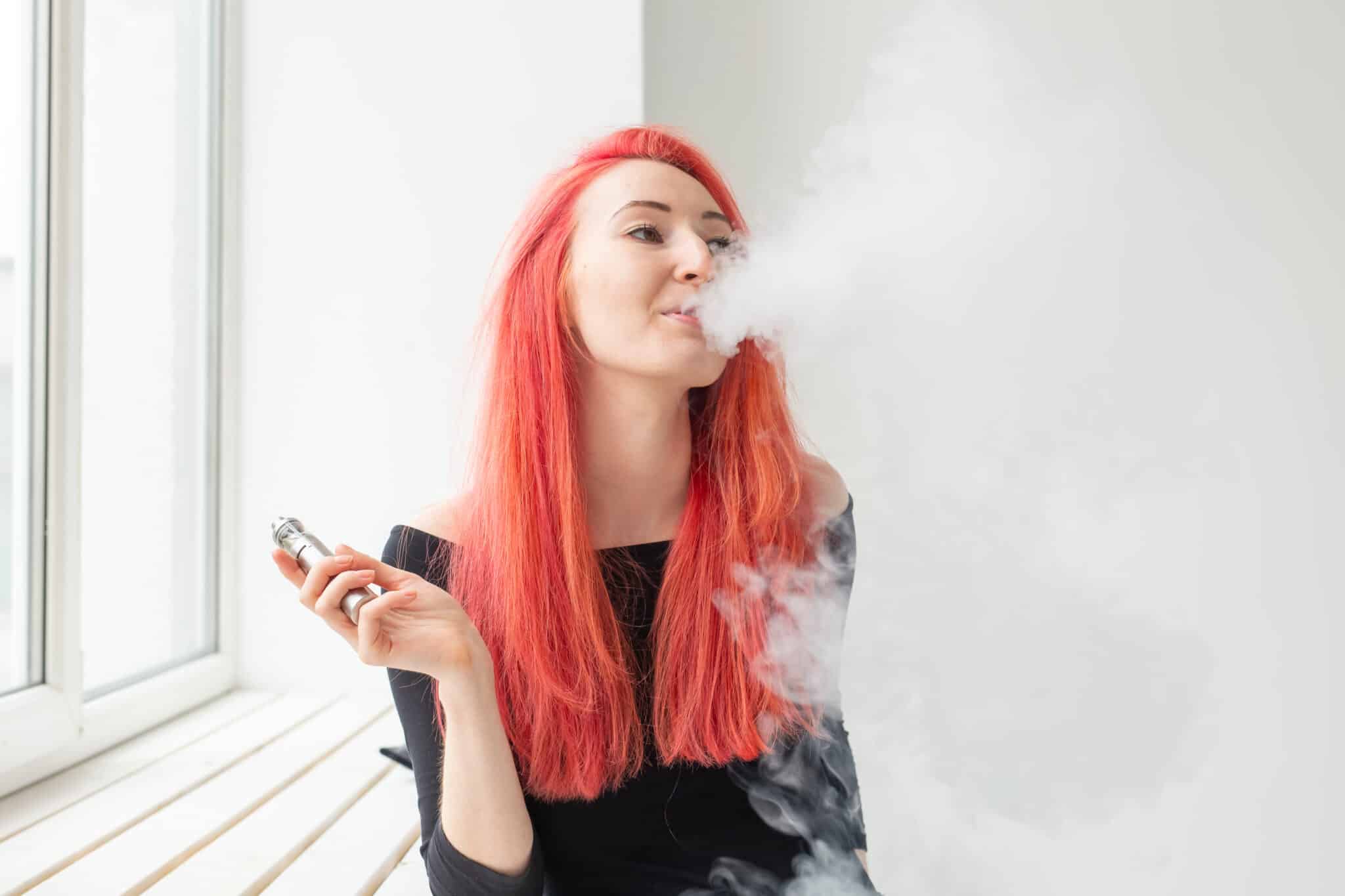 youth addiction concept young red haired woman smoking vape near window 2048x1365 1 de pe e-potion.ro